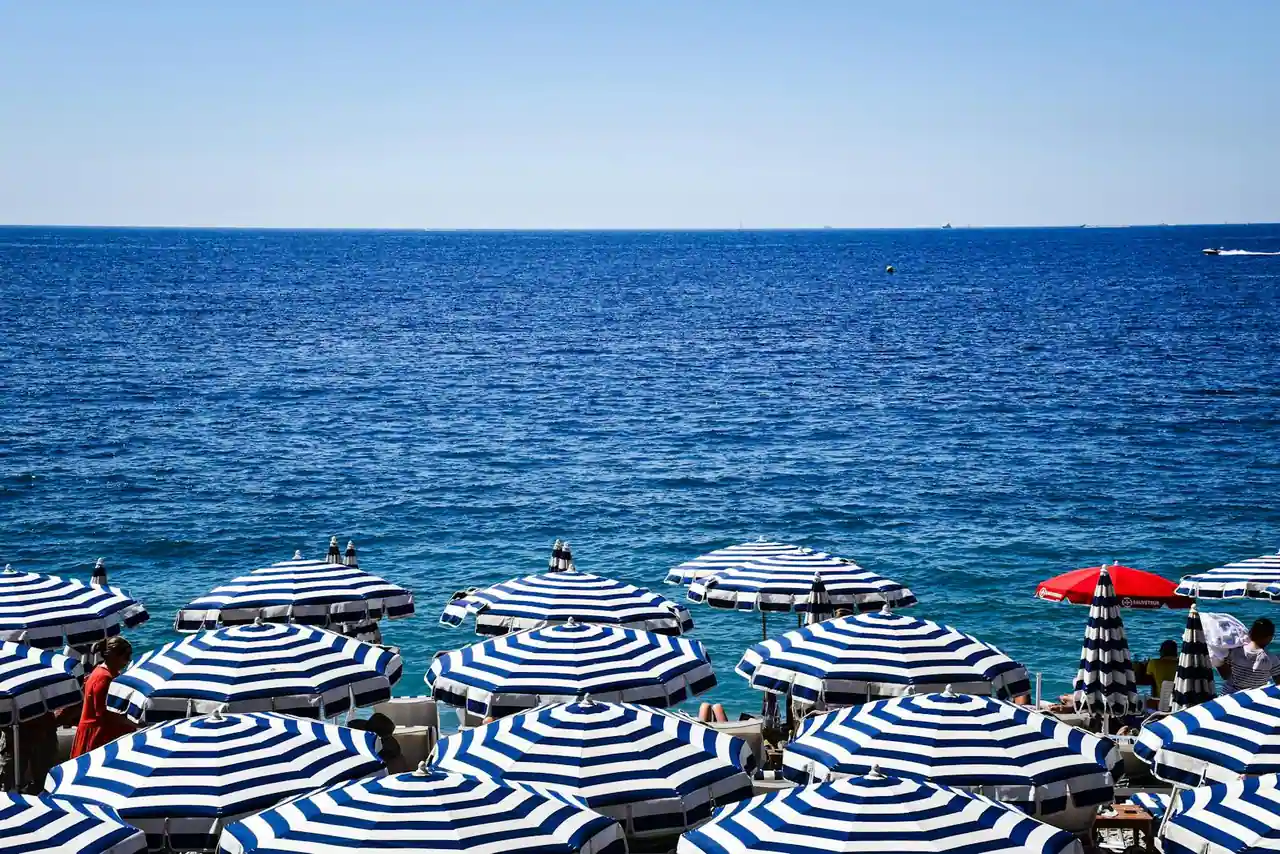 Terrasse d'hôtel pieds dans l'eau sur la Côte d'Azur en fin de journée, méditerranée au premier plan, pins maritimes.