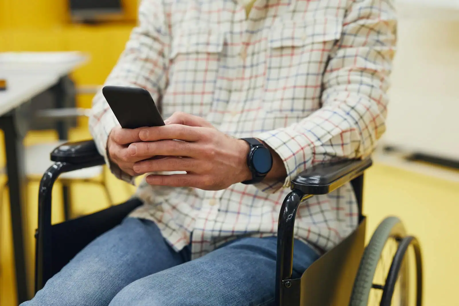 Personne en fauteuil roulant consultant un smartphone dans un espace urbain accessible