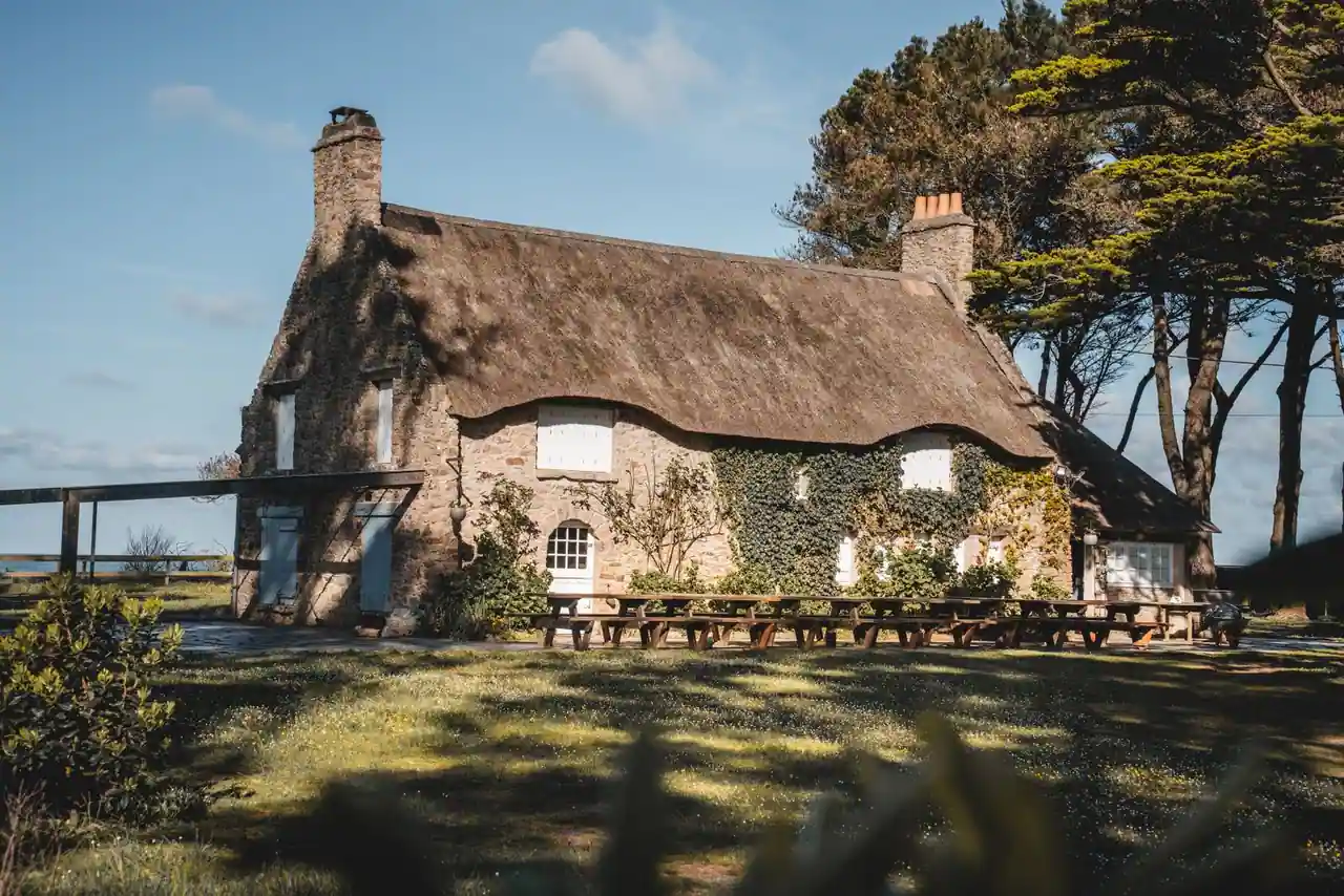 Gîte traditionnel en pierre au bord du littoral breton, ciel changeant et façade fleurie
