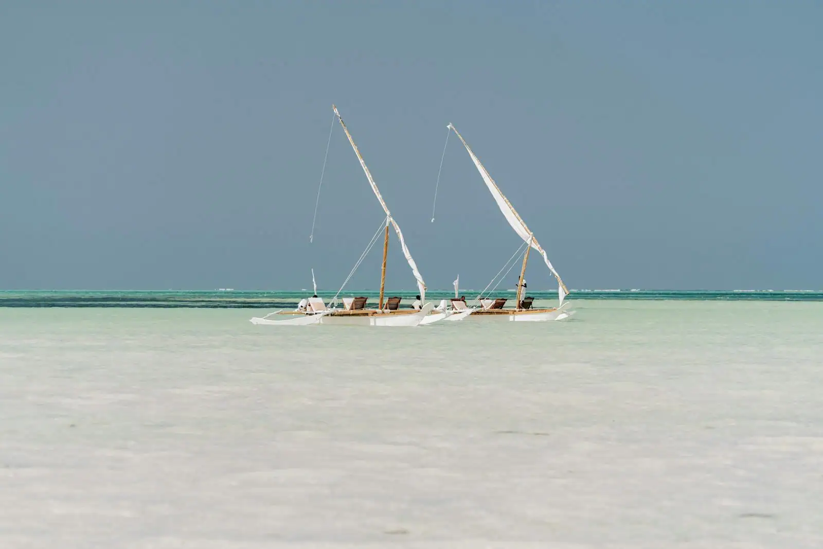 Plage de sable blanc à Zanzibar avec eau turquoise et bateau traditionnel dhow à l'horizon