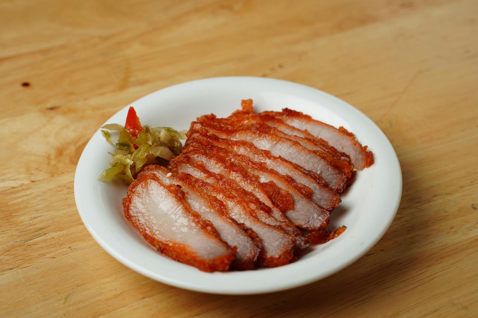 Rôti de porc tranché sur une planche en bois, jus brun en saucière, lumière naturelle de cuisine