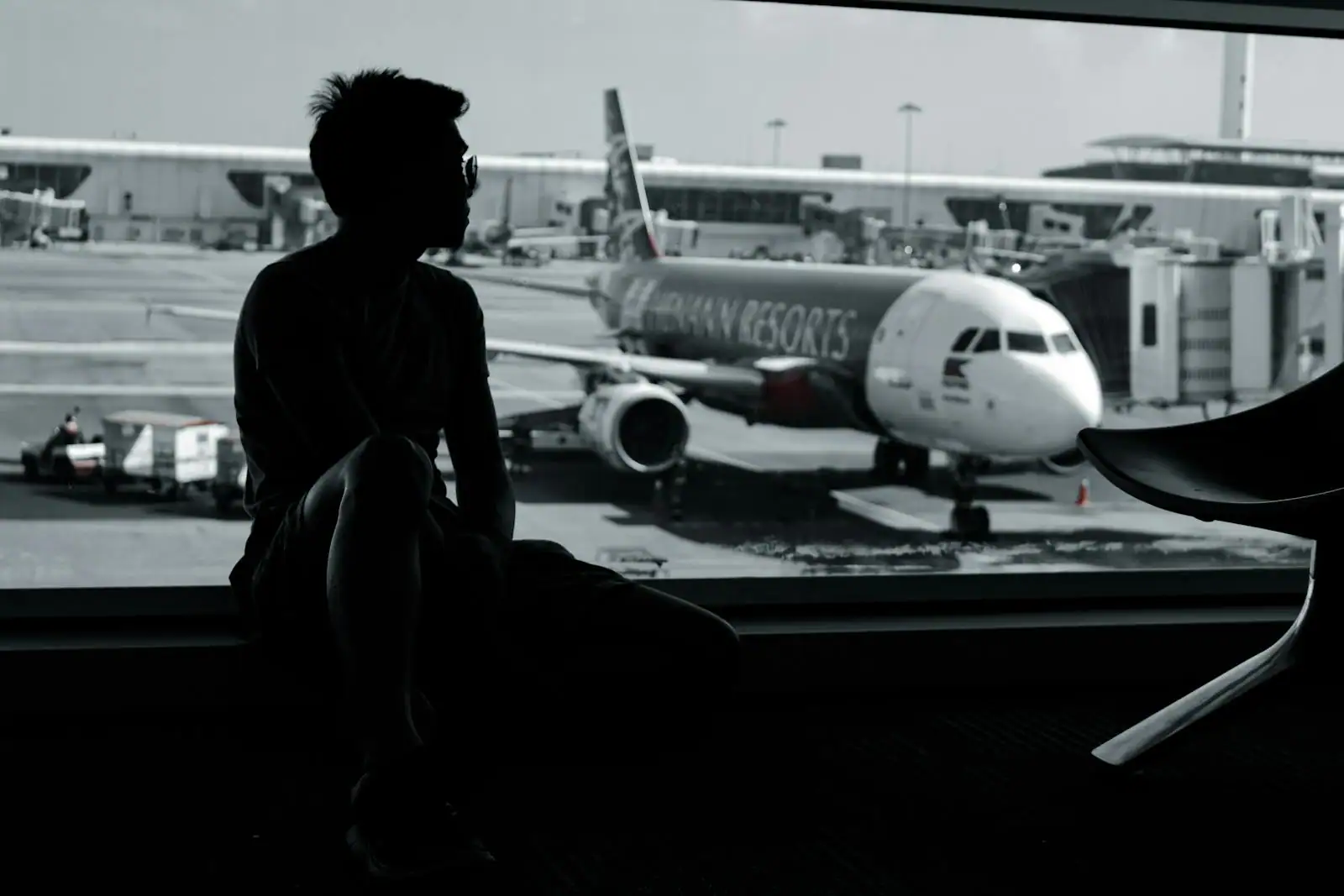 Voyageur en silhouette observant un avion de ligne à la porte d'embarquement, depuis le terminal.