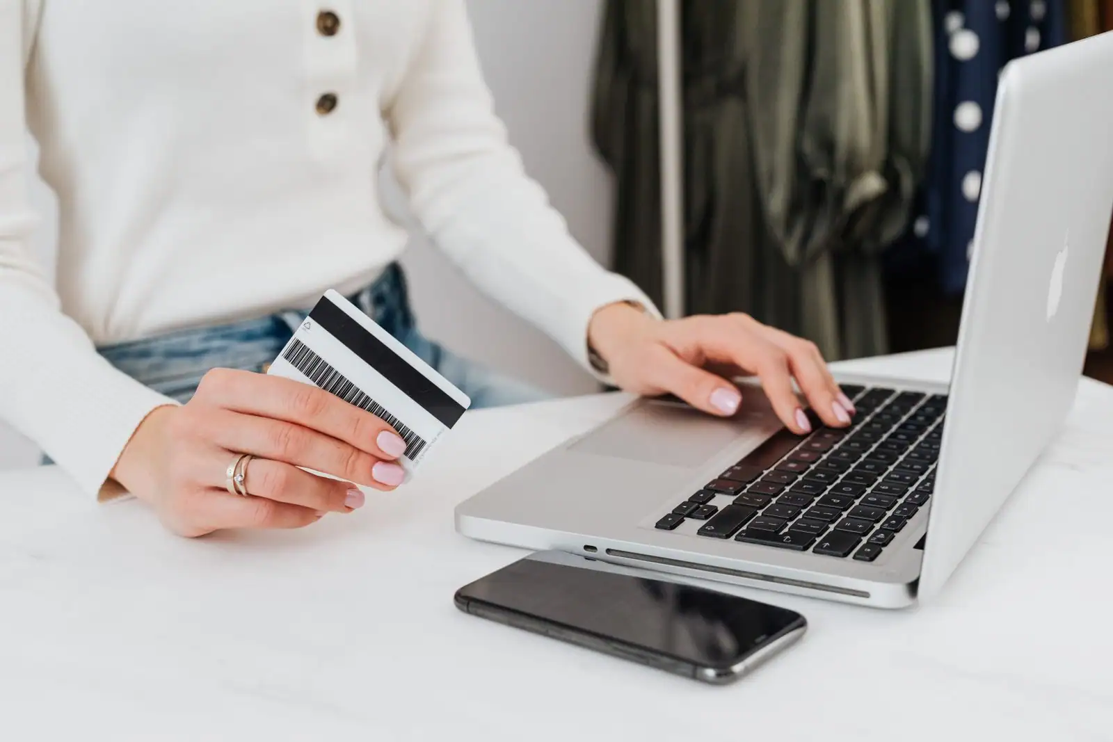 Une personne fait des achats de vêtements en ligne sur un ordinateur portable, carte bancaire à la main