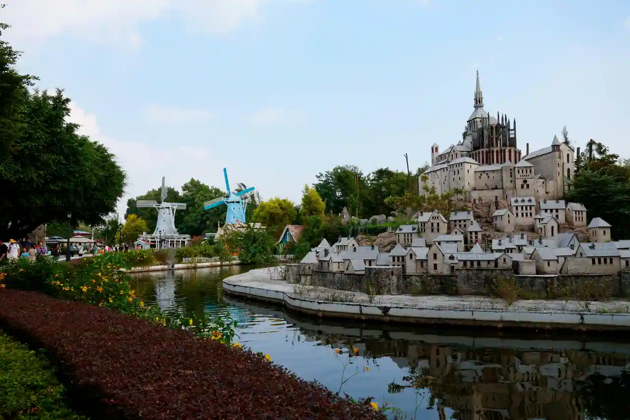 Maquettes dans un parc de miniatures : une abbaye perchée, un village et des moulins au bord d'un bassin.