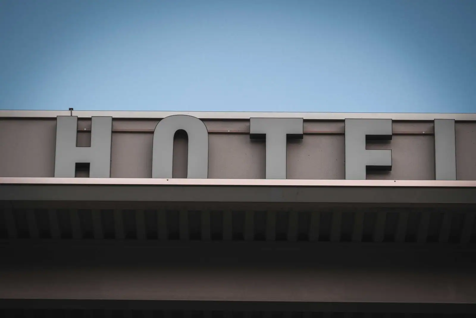 Enseigne « HOTEL » sur la façade d'un bâtiment, vue en contre-plongée sous un ciel bleu.