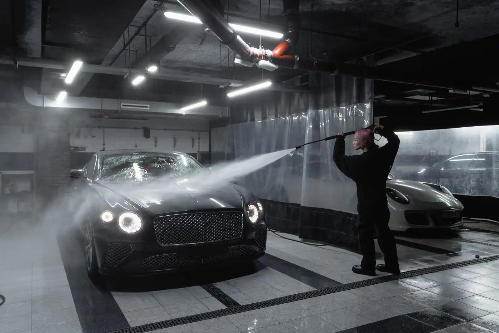 Personne nettoyant une voiture au jet d'un nettoyeur haute pression dans un box de lavage