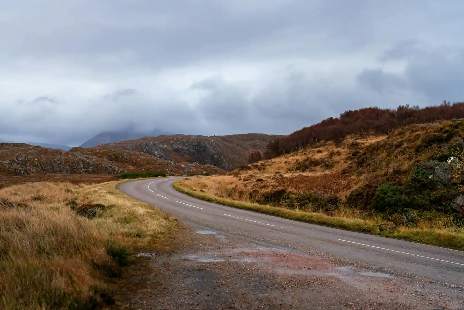 Route sinueuse traversant les landes des Highlands écossais sous un ciel nuageux