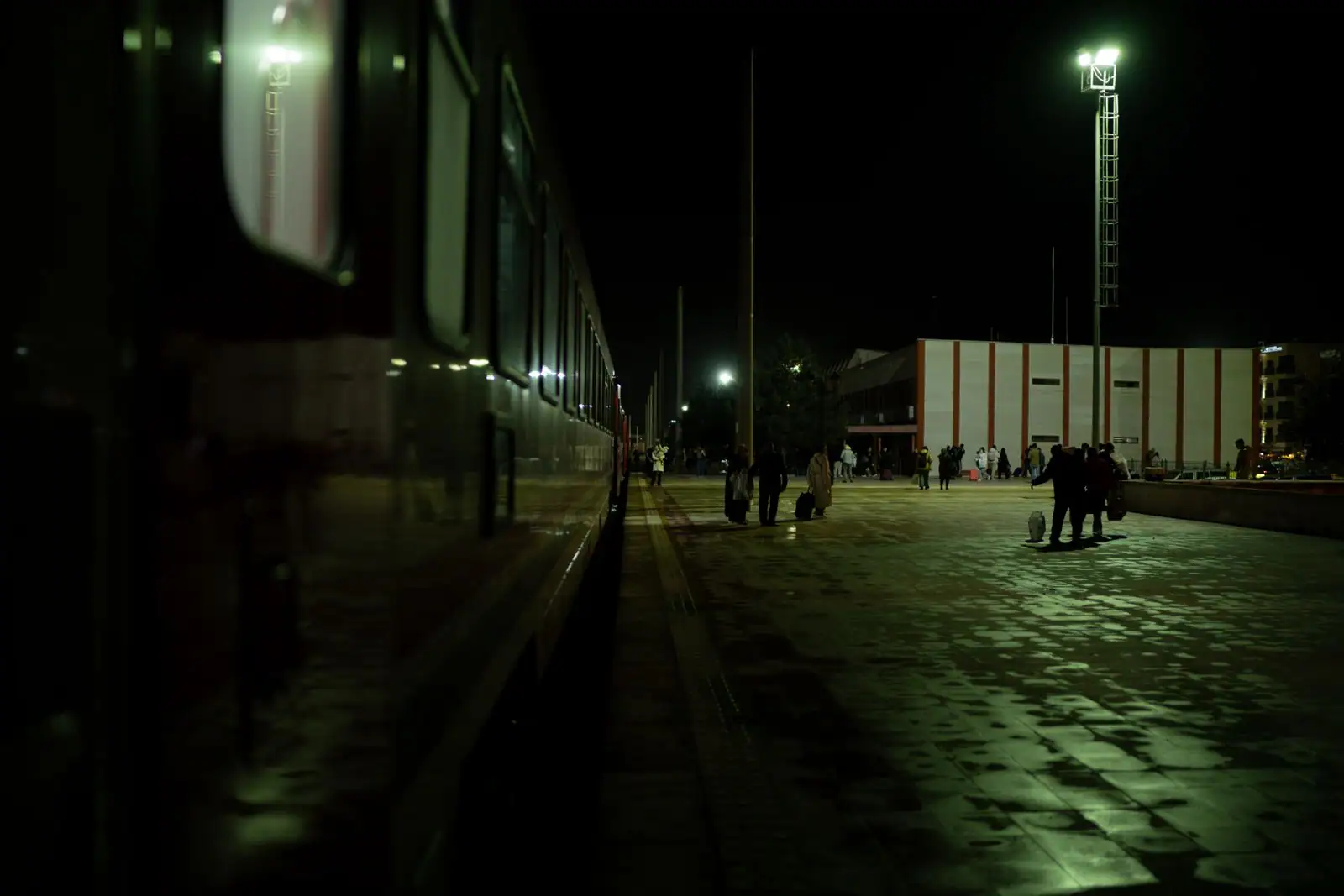Train à quai dans une gare faiblement éclairée la nuit, des voyageurs sur le quai