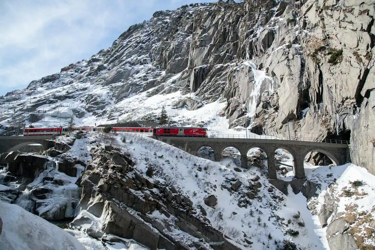 Train rouge franchissant un viaduc en pierre dans un paysage de montagne enneigé des Alpes suisses
