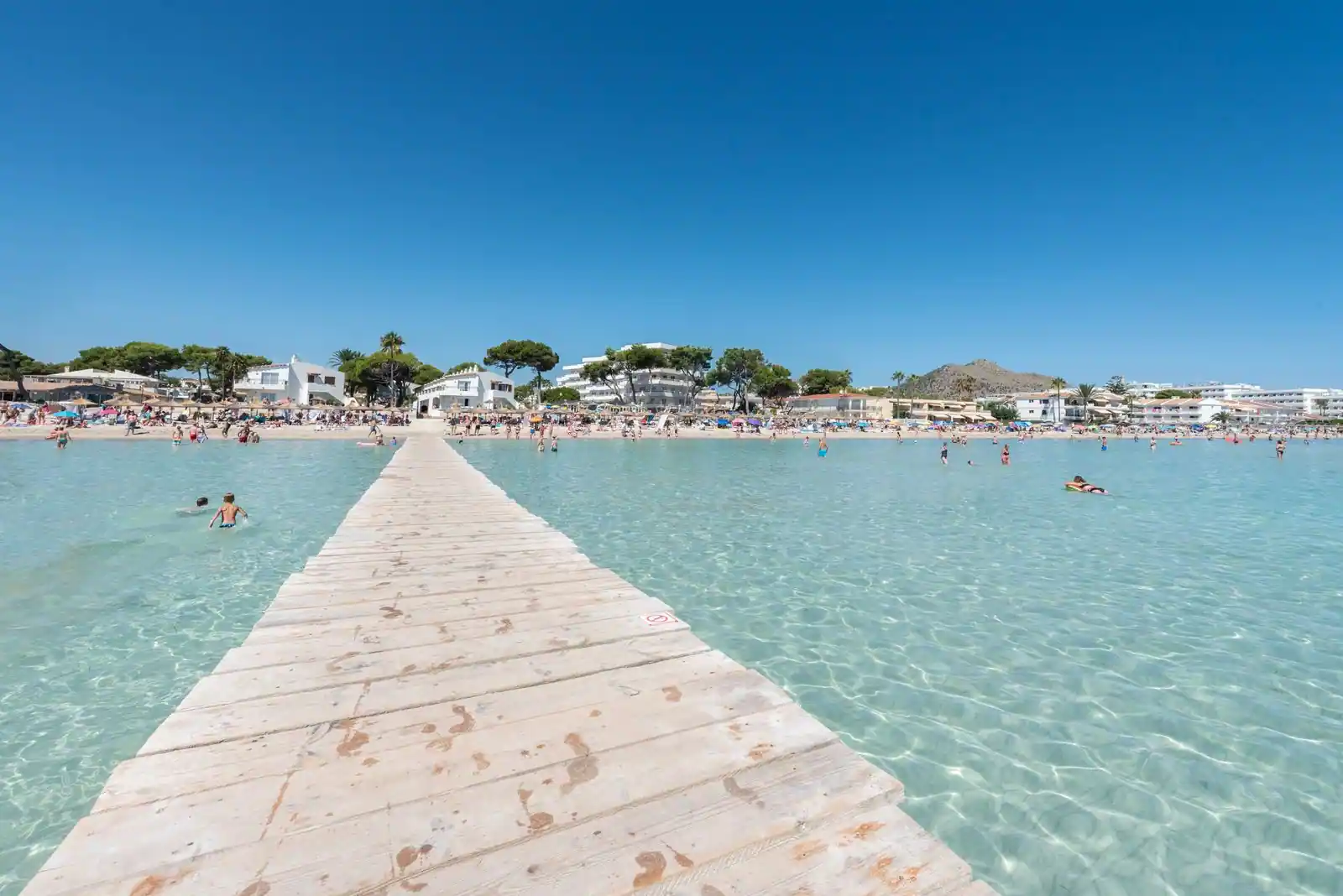 Ponton de bois s'avançant sur des eaux turquoise peu profondes, plage familiale d'Alcúdia à Majorque