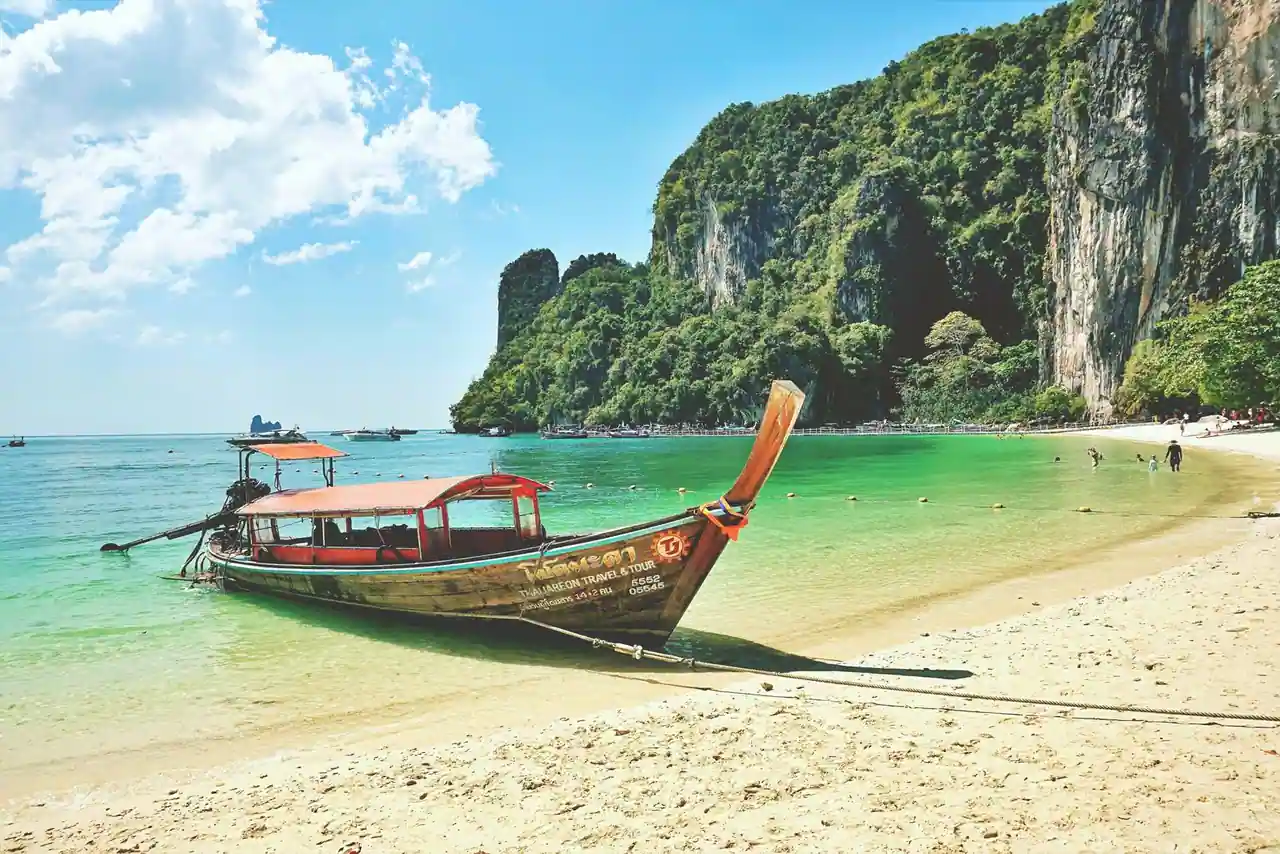 Bateau à longue queue sur une eau turquoise devant des falaises calcaires en Thaïlande