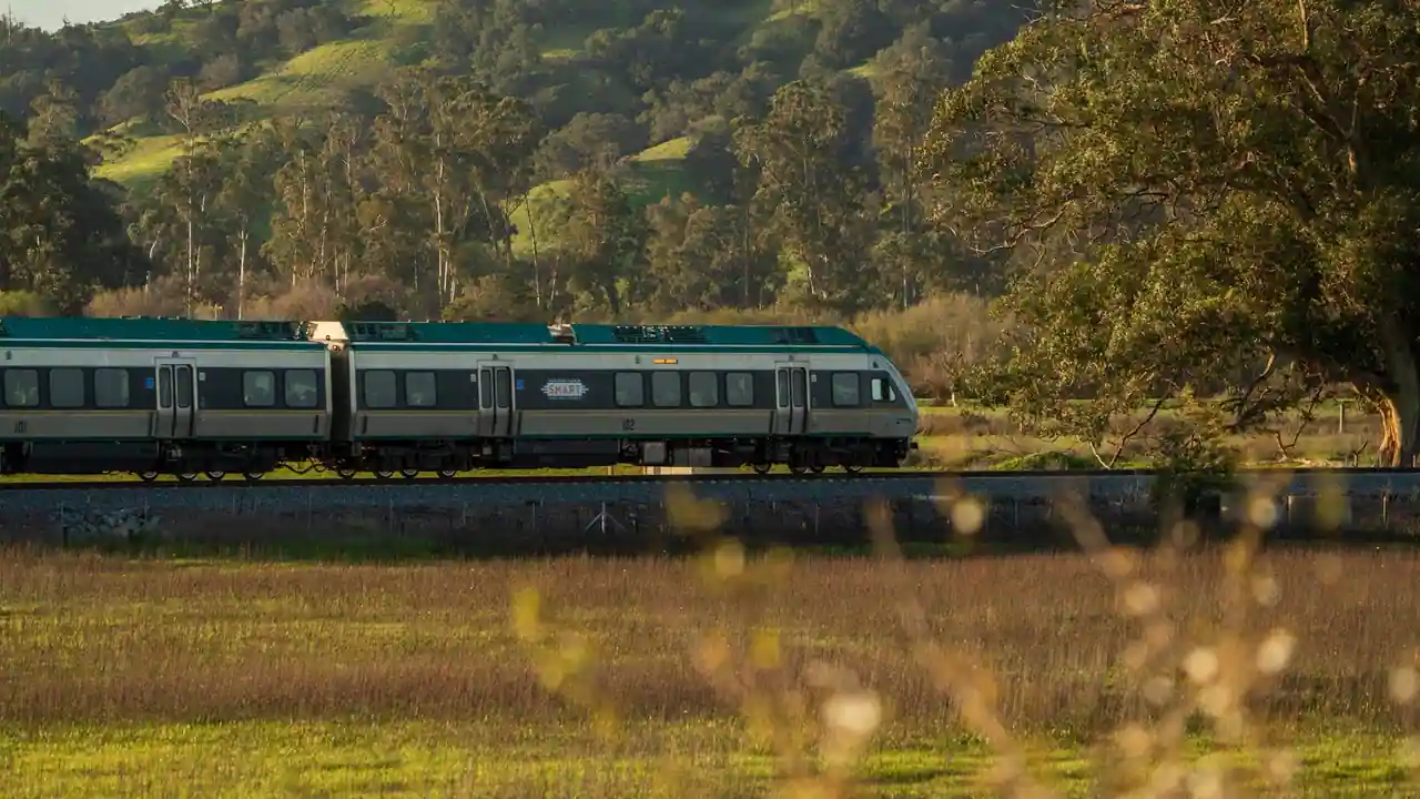 Train de voyageurs traversant une campagne verdoyante au pied des collines