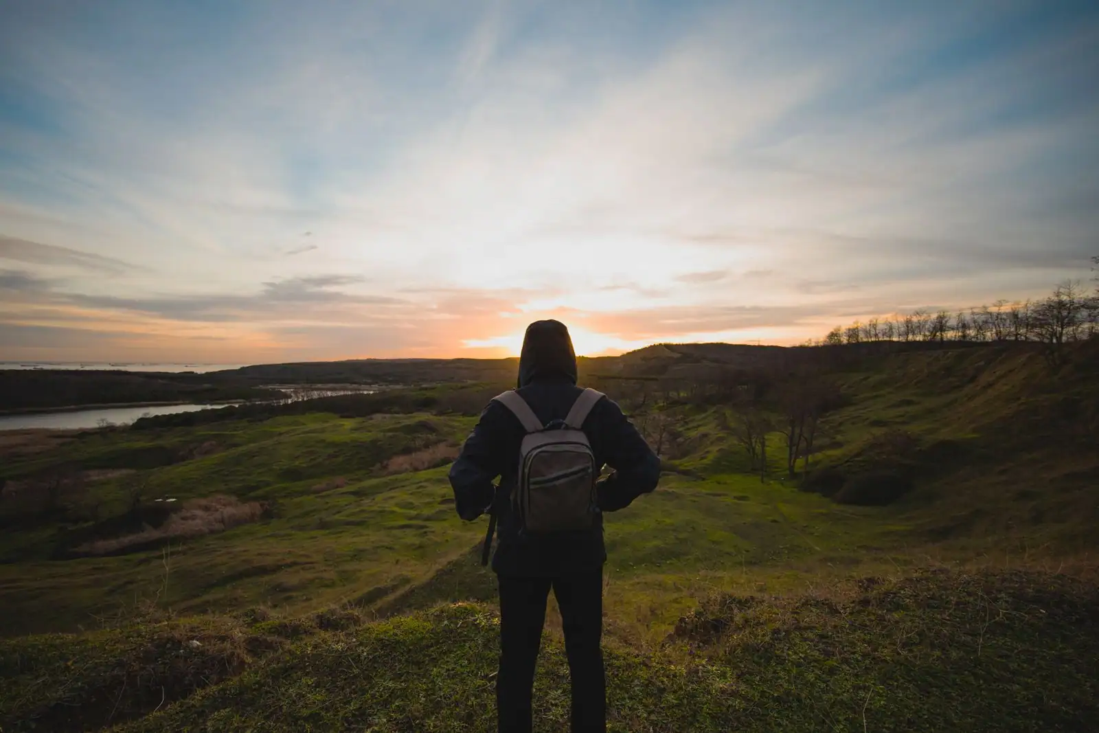 Voyageur avec un sac à dos face à un large paysage ouvert au lever du jour