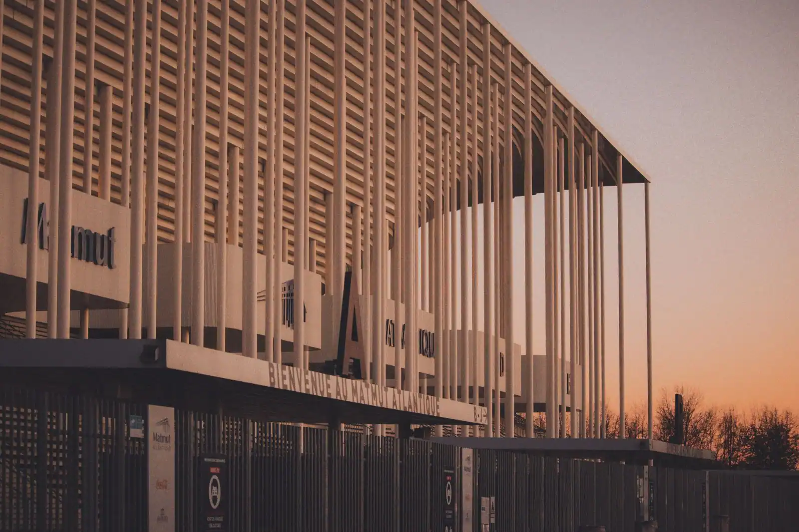 Façade à colonnes et grilles d’entrée du stade Matmut Atlantique, à Bordeaux, au coucher du soleil.