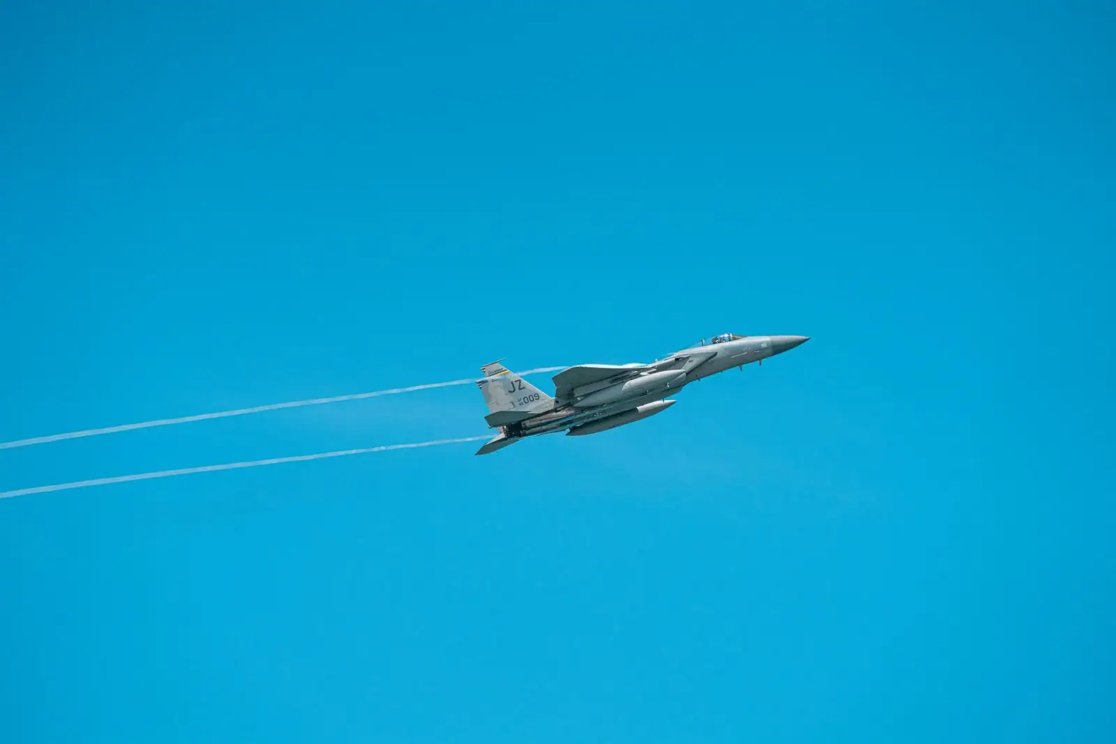 Avion de chasse militaire en vol dans un ciel bleu dégagé, laissant des traînées de condensation