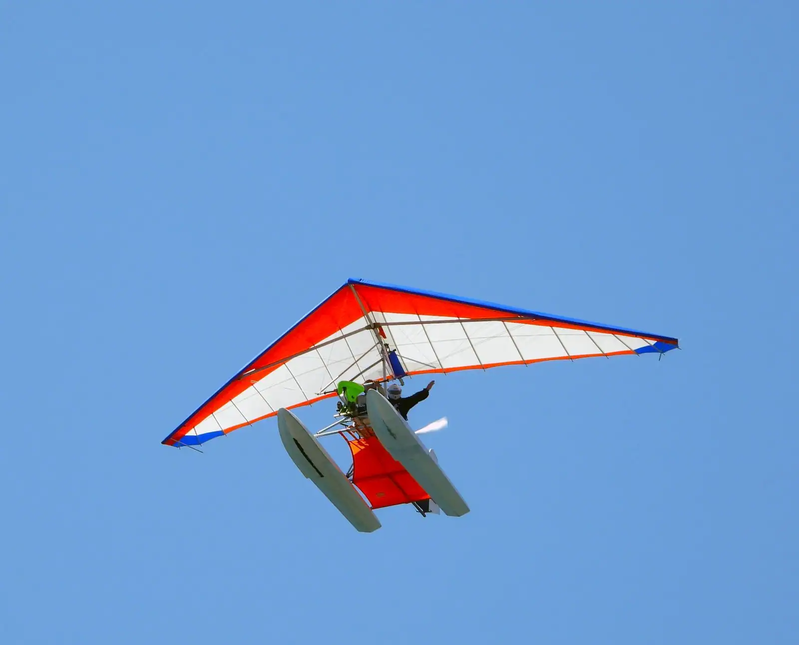 ULM pendulaire aux couleurs vives en vol dans un ciel bleu, aile souple et hélice bien visibles.