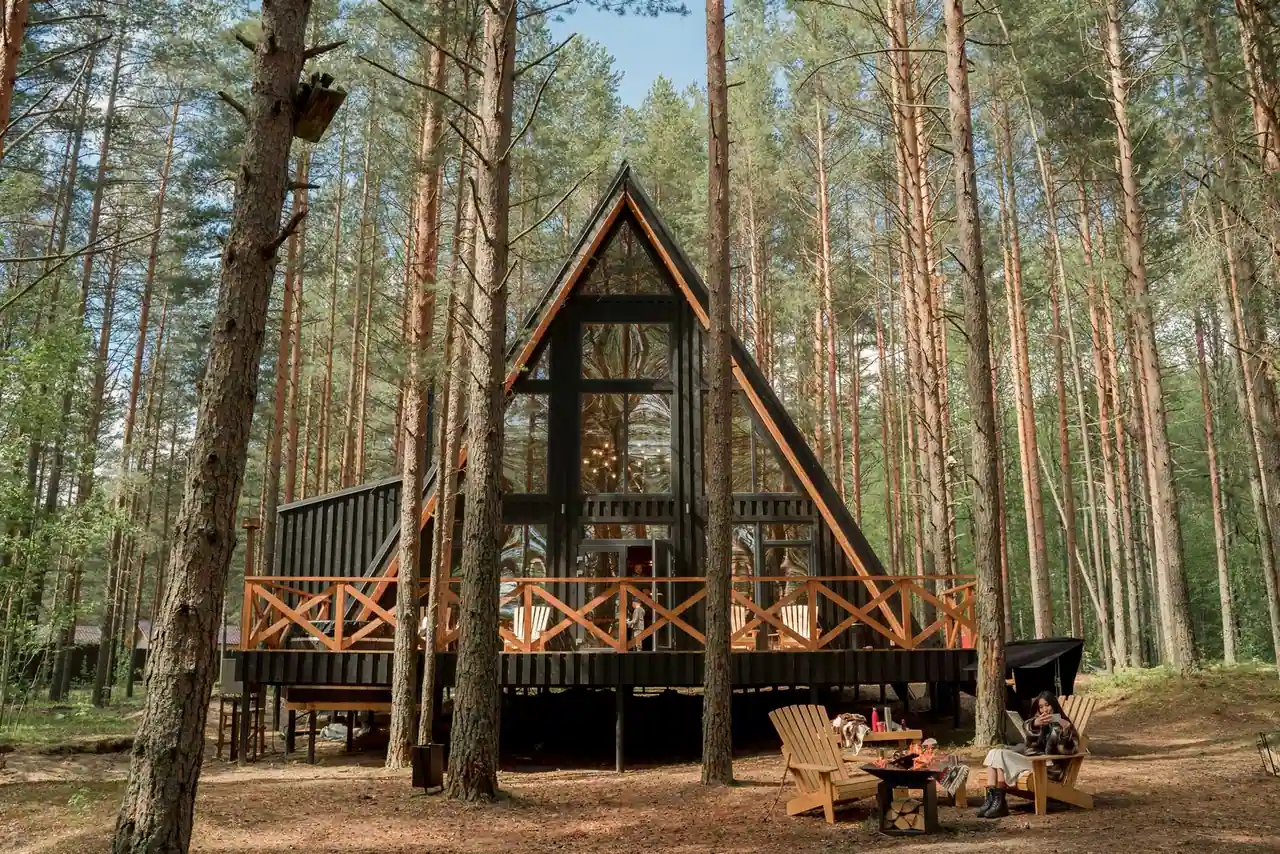 Chalet en bois triangulaire niché parmi les pins, avec terrasse et transats, hébergement insolite de plein air.