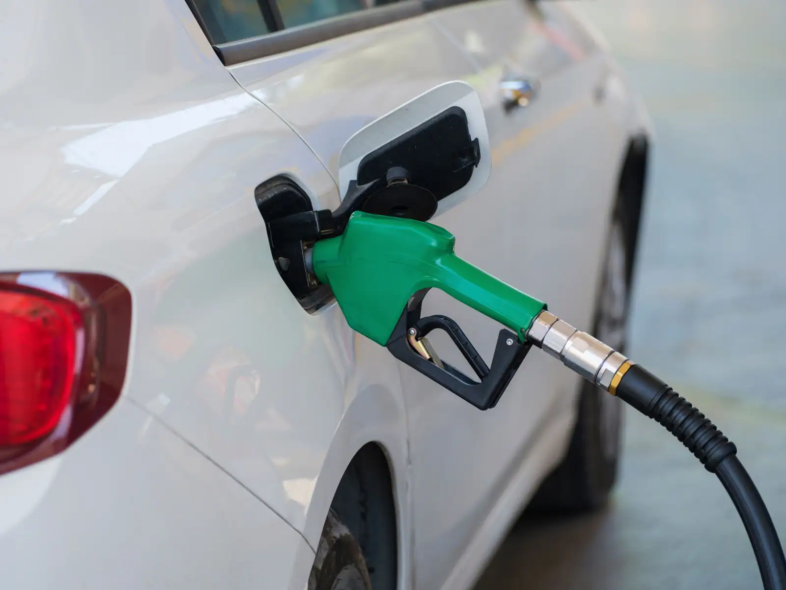Pistolet vert inséré dans le réservoir d'une voiture blanche pour faire le plein de carburant.