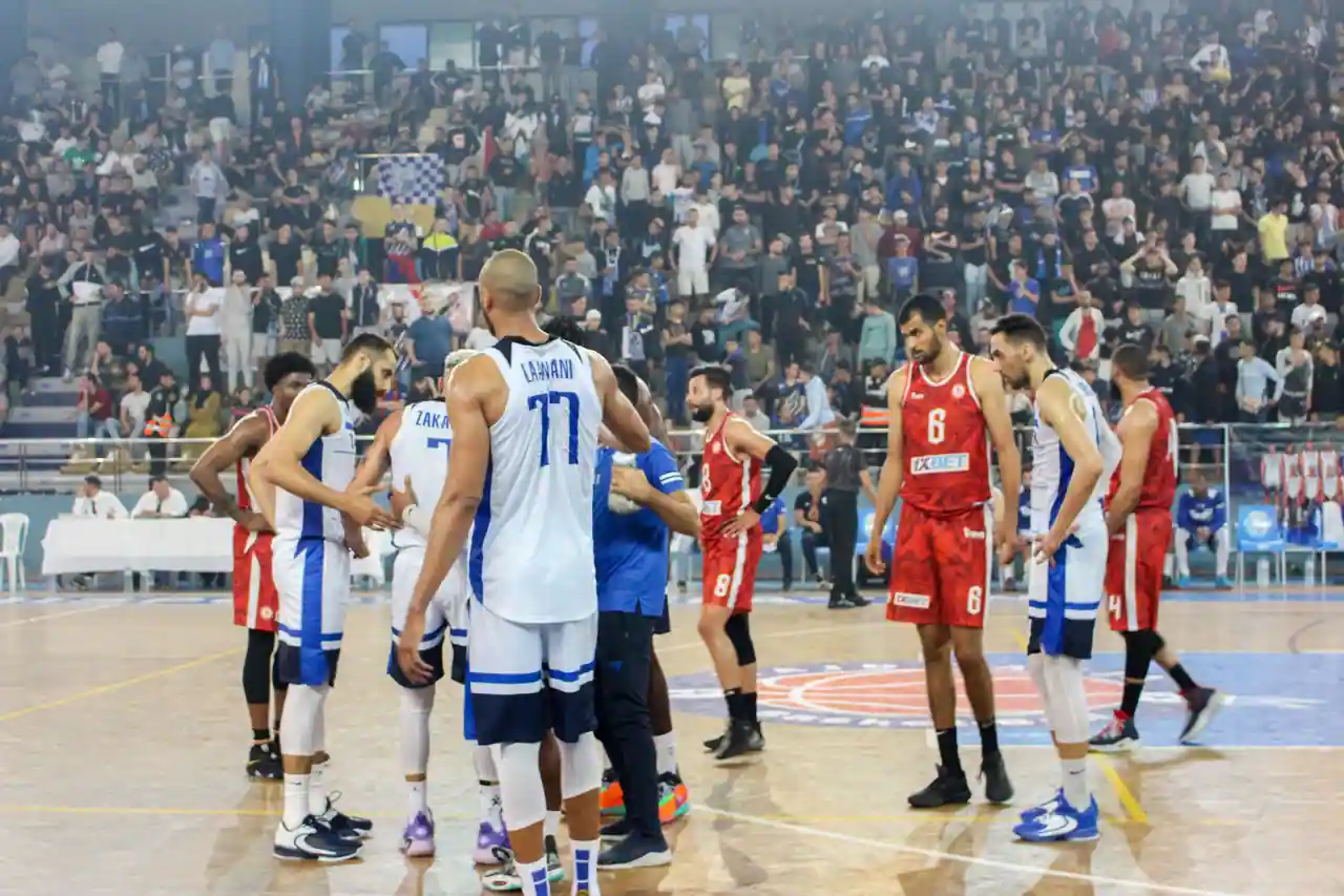 Joueurs de basket-ball rassemblés sur le parquet lors d'un match, devant des tribunes pleines.
