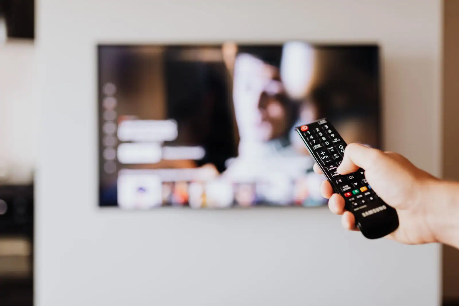 Personne tenant une télécommande devant un téléviseur allumé dans un salon