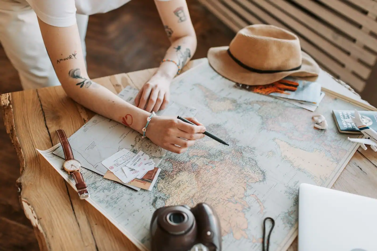 Voyageuse pointant une destination sur une carte du monde, passeport et chapeau posés sur la table