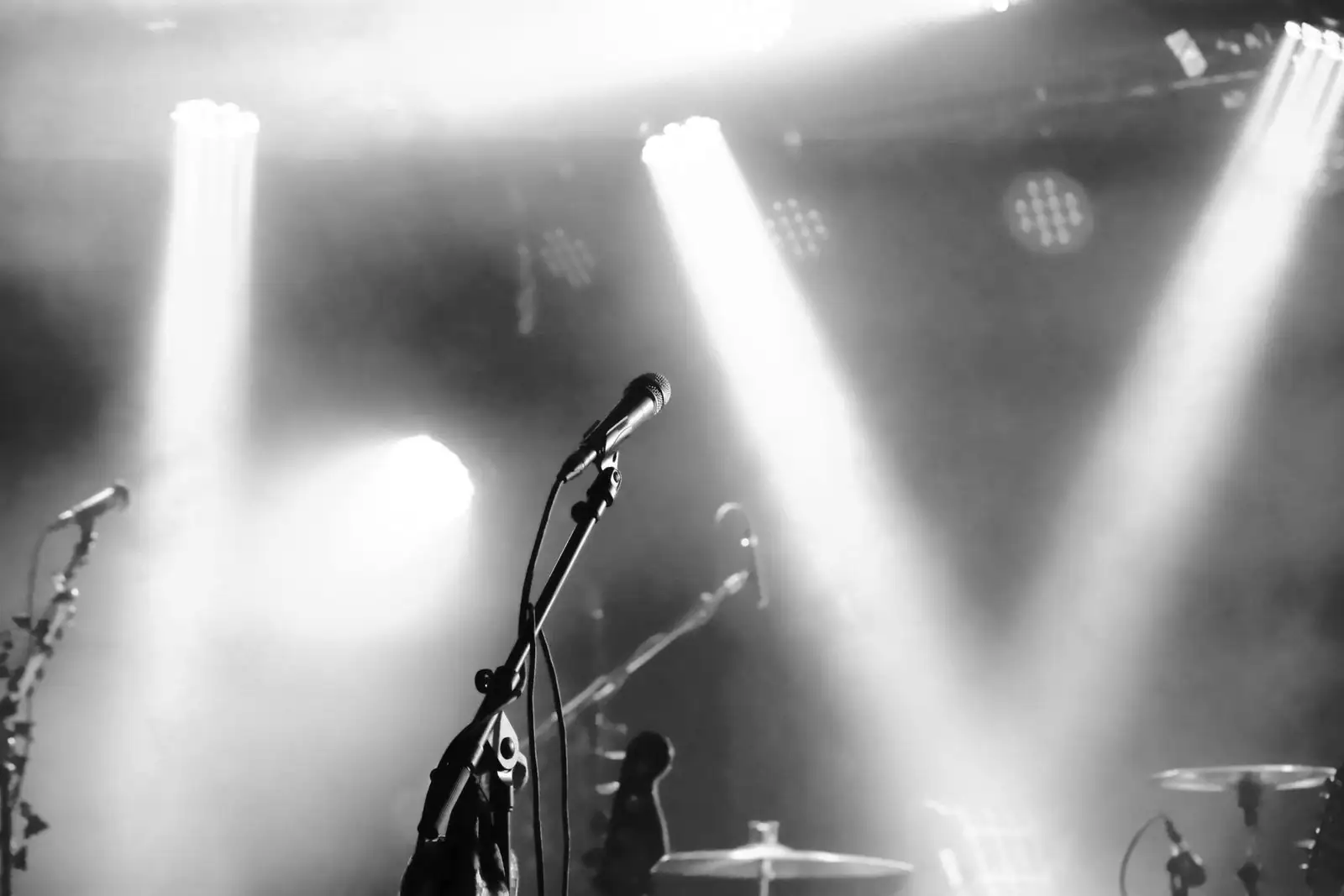 Micro de chant sur pied devant une scène de concert éclairée par des projecteurs, en noir et blanc