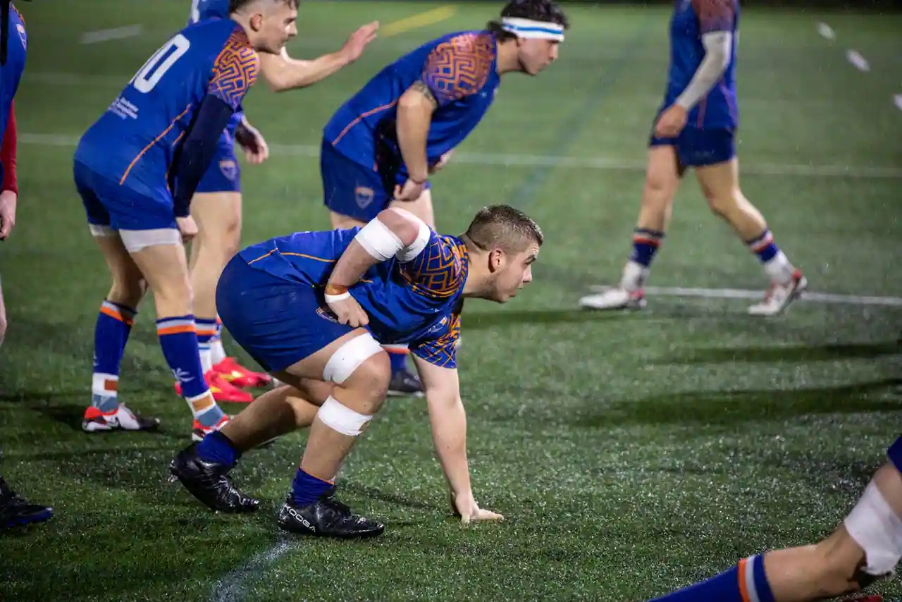 Joueurs de rugby en action lors d'un match sur la pelouse d'un stade, en soirée.