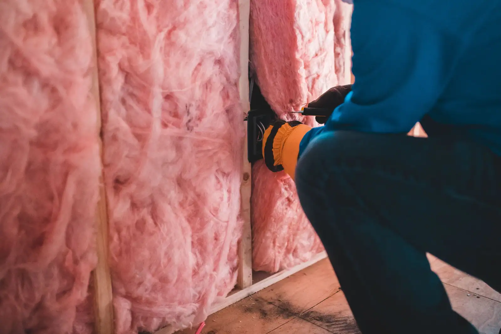 Un ouvrier ganté pose de la laine minérale entre les montants d'une cloison, pendant des travaux d'isolation.