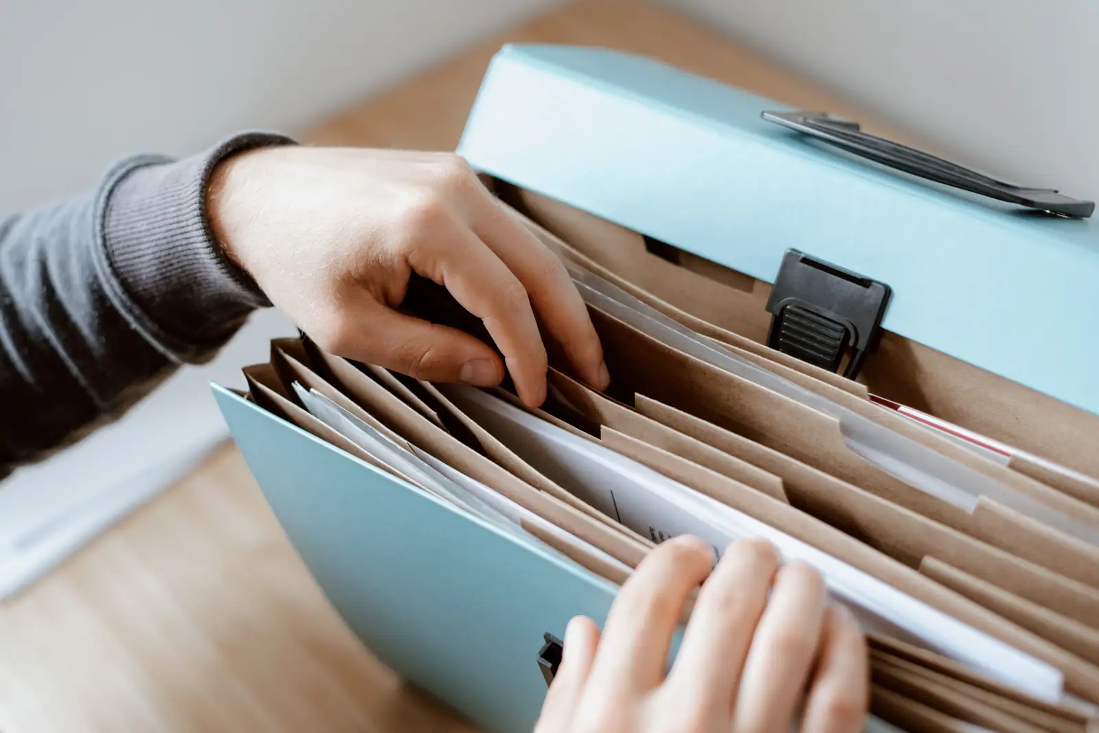 Mains cherchant un justificatif dans un trieur à soufflets rempli de documents administratifs.