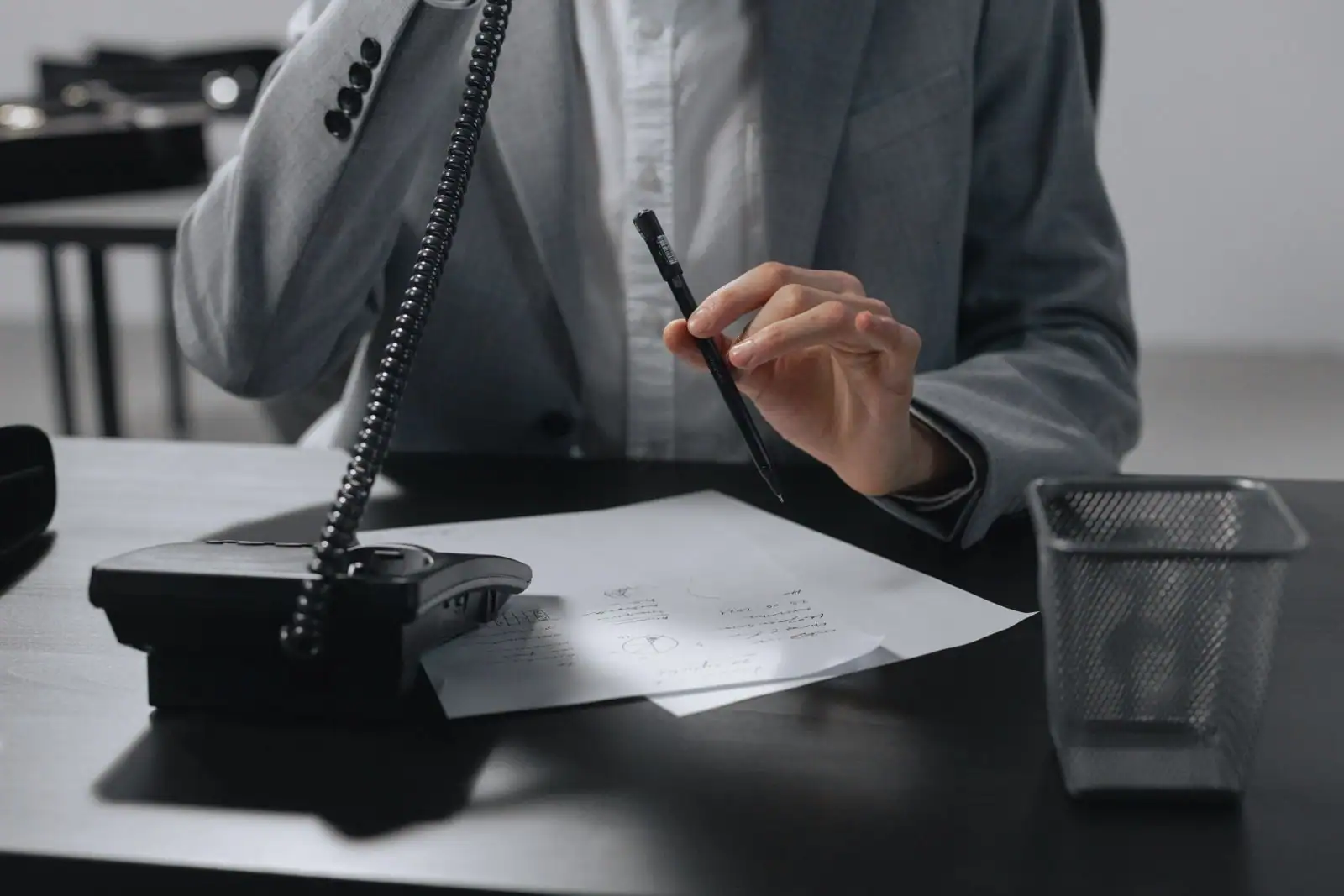 Personne au téléphone à un bureau, combiné à l'oreille, prenant des notes au stylo