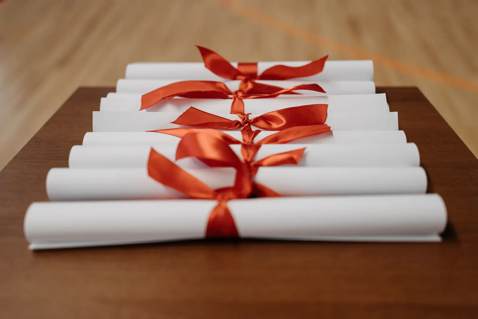 Diplômes roulés fermés par des rubans orange, posés sur un bureau en bois