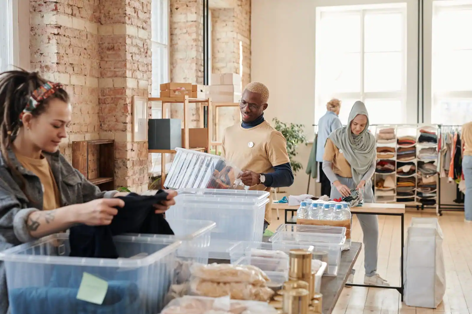 Des bénévoles trient vêtements et denrées dans de grands bacs, au sein d’un local associatif lumineux