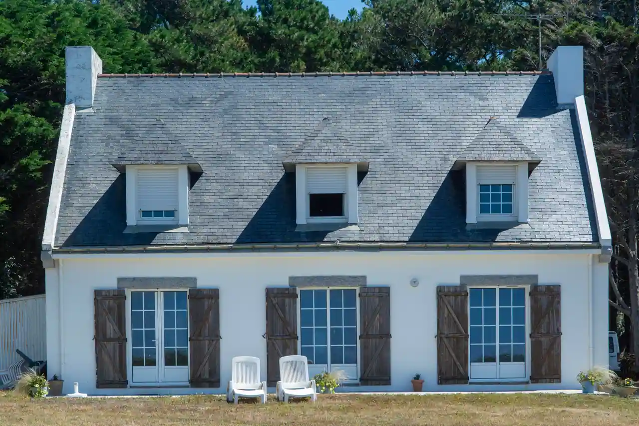 Une maison de vacances à toit d'ardoise et volets en bois, dans le style breton, avec des chaises de jardin