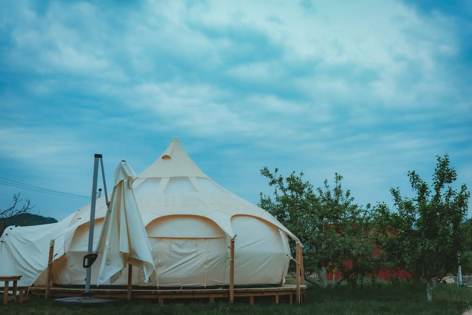 Grande tente de glamping en toile claire, montée sur un plancher en bois dans un cadre de verdure