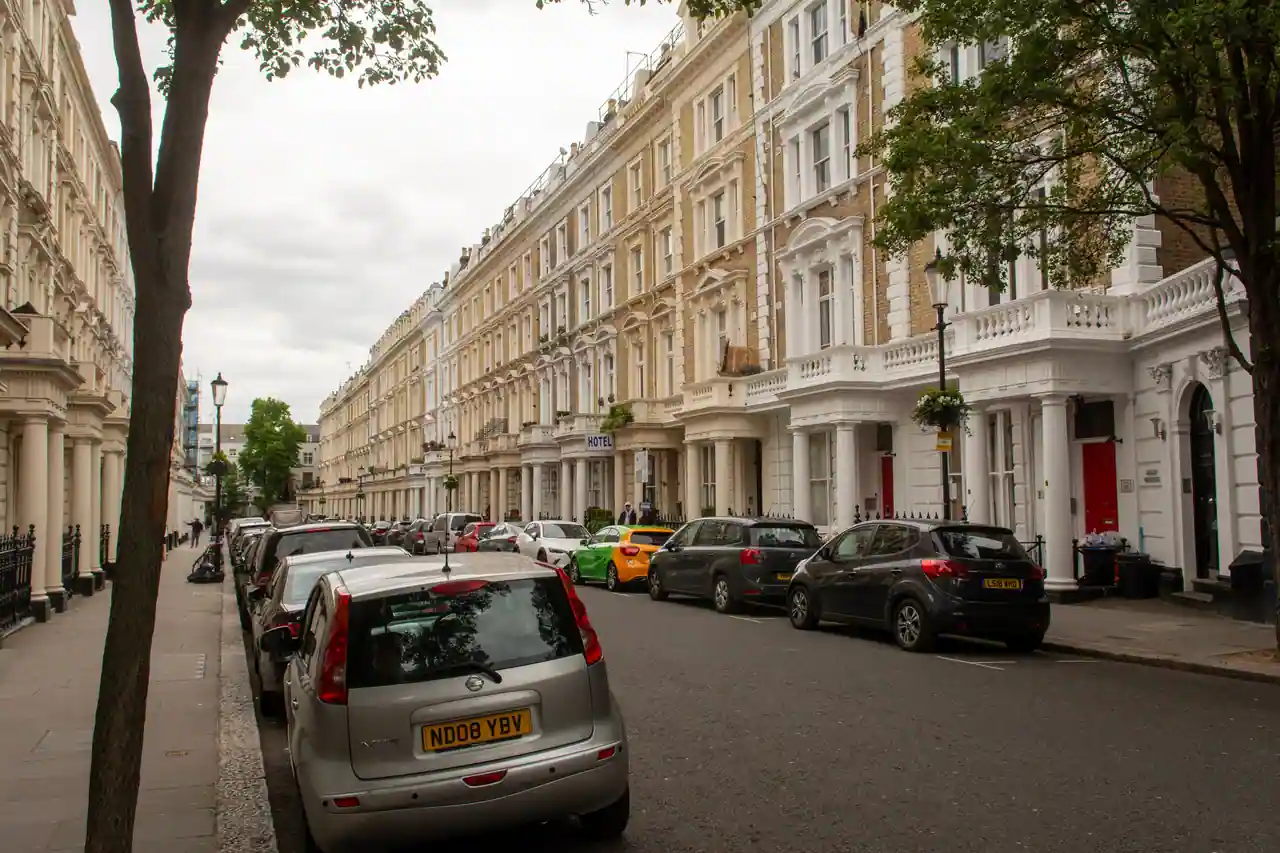 Rue londonienne bordée de maisons victoriennes, dont l'une porte l'enseigne d'un petit hôtel.