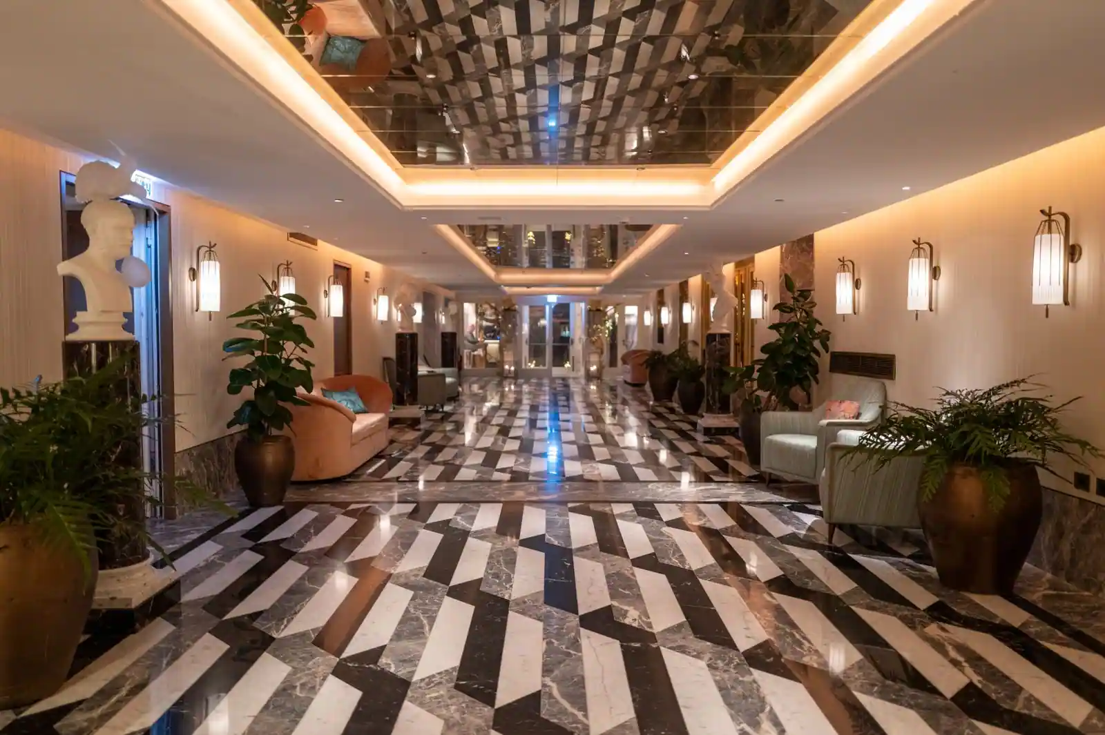 Long hall d'un hôtel haut de gamme au sol de marbre à motifs géométriques noir et blanc, éclairé par des appliques