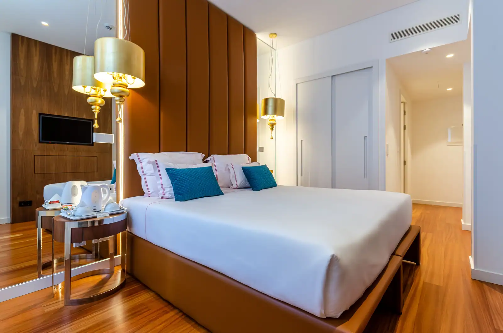 Chambre d'hôtel moderne avec un grand lit blanc, une tête de lit capitonnée et des lampes dorées