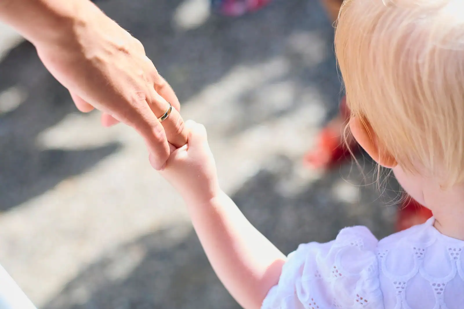 Un parent tenant la main de son jeune enfant à l'extérieur, image illustrant une famille