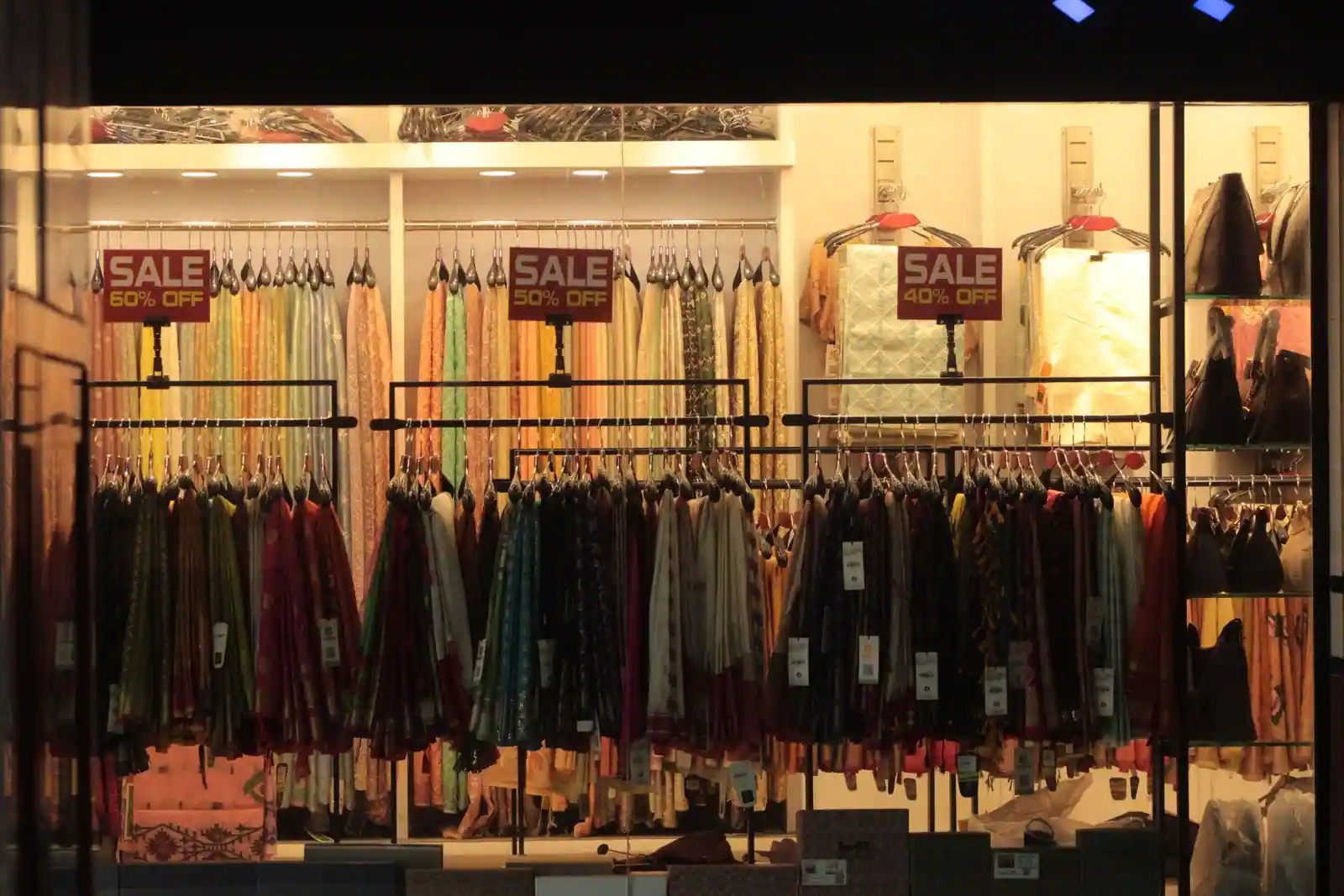 Rayons d'une boutique de vêtements éclairée, avec des panneaux « SALE » et des pourcentages de réduction.