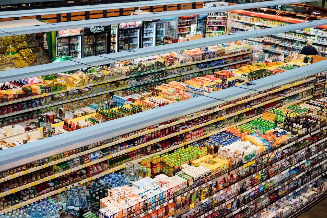Vue en plongée sur les rayons garnis d’un supermarché, aux nombreux produits alimentaires colorés.