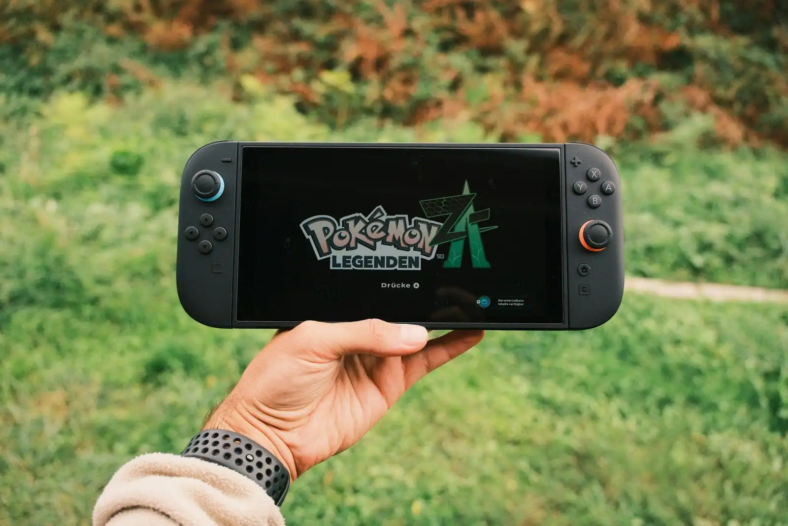 Console de jeu vidéo portable tenue à la main en extérieur, affichant l'écran-titre d'un jeu vidéo