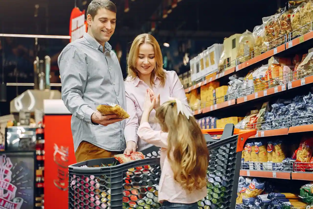Une famille fait ses courses dans une allée de supermarché, un chariot rempli devant les rayons