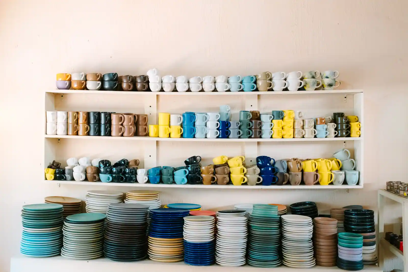 Tasses et assiettes en céramique colorées empilées sur des étagères dans un magasin d'articles pour la maison.