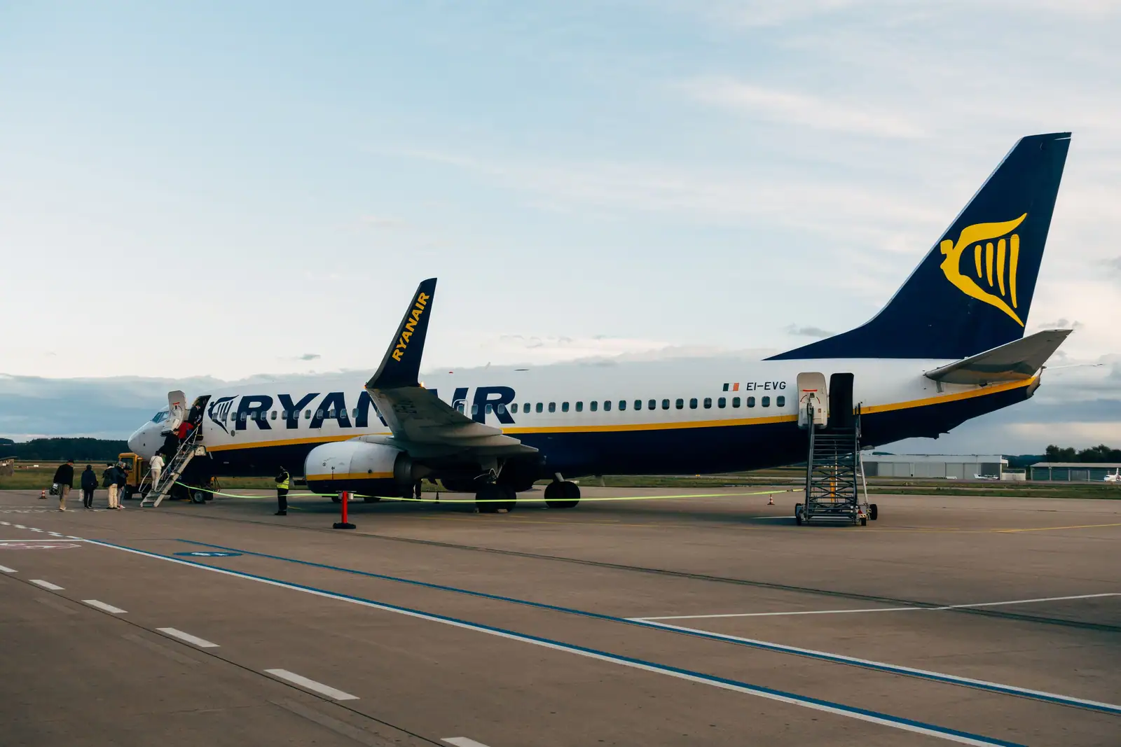 Avion Ryanair stationné sur le tarmac d'un aéroport, passerelle déployée et passagers en cours d'embarquement
