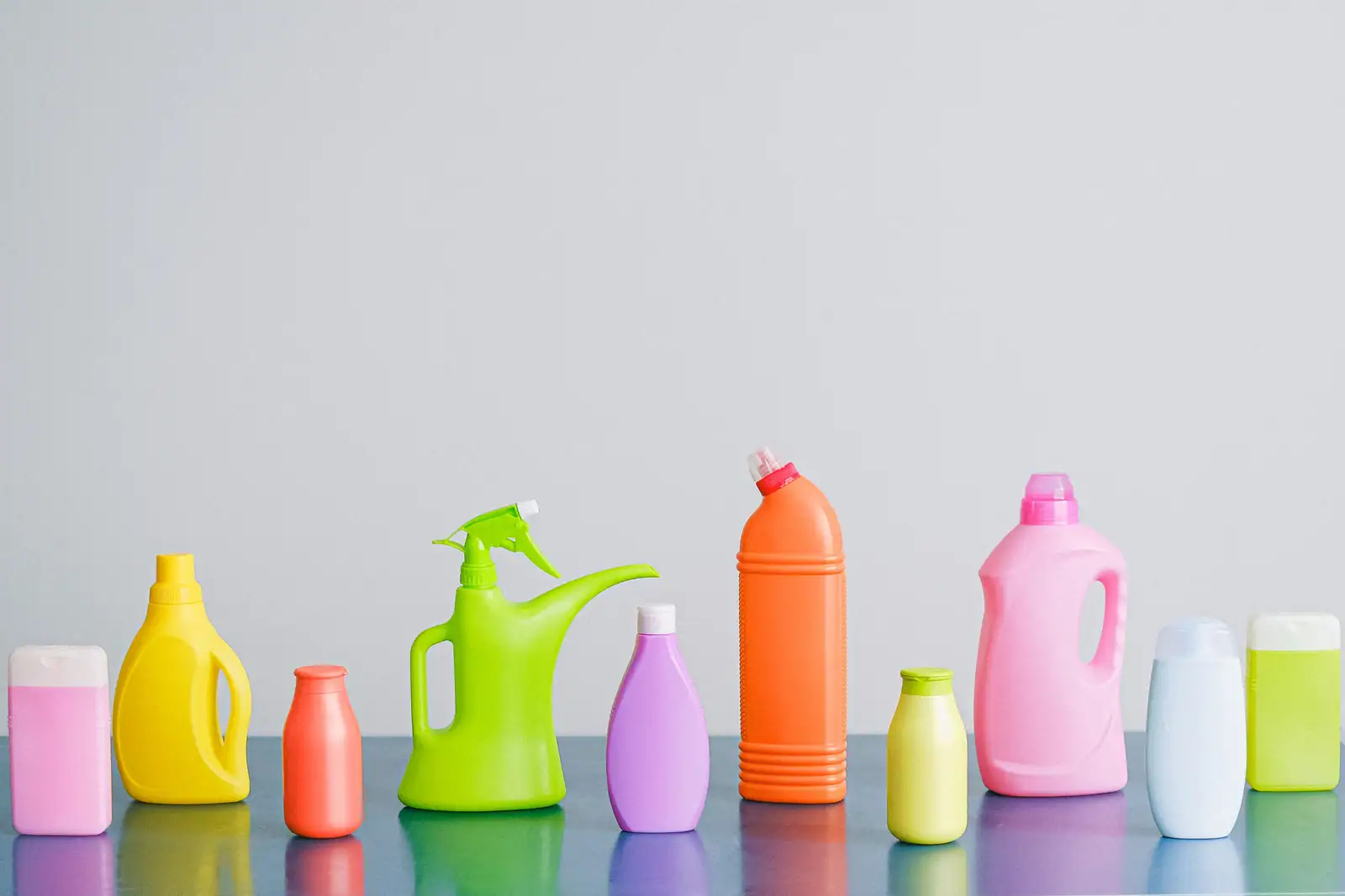 Rangée de produits d'entretien ménager colorés en flacons plastique alignés sur fond clair.