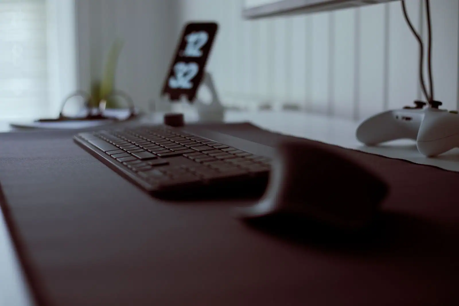 Bureau avec clavier et manette de jeu vidéo posés sur un tapis, dans une lumière tamisée