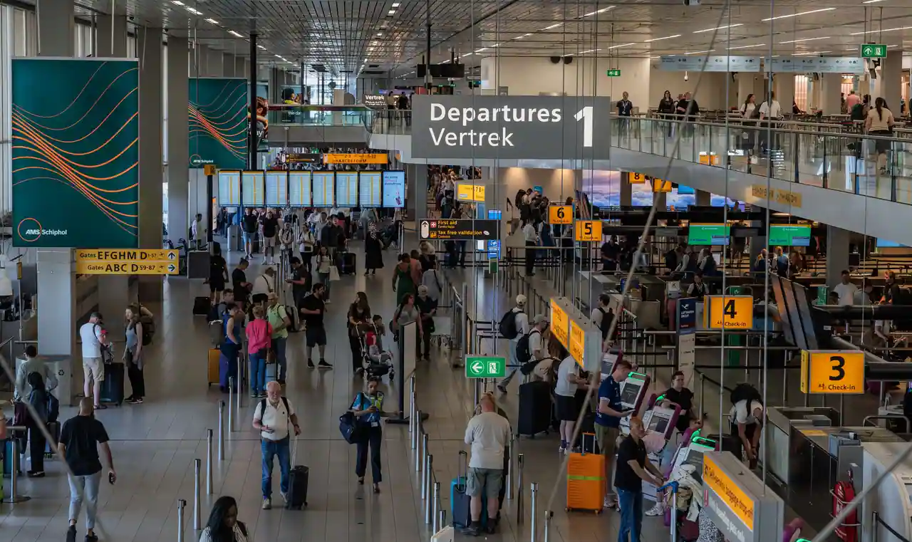 Hall des départs de l'aéroport d'Amsterdam-Schiphol : comptoirs d'enregistrement, écrans de vols et voyageurs