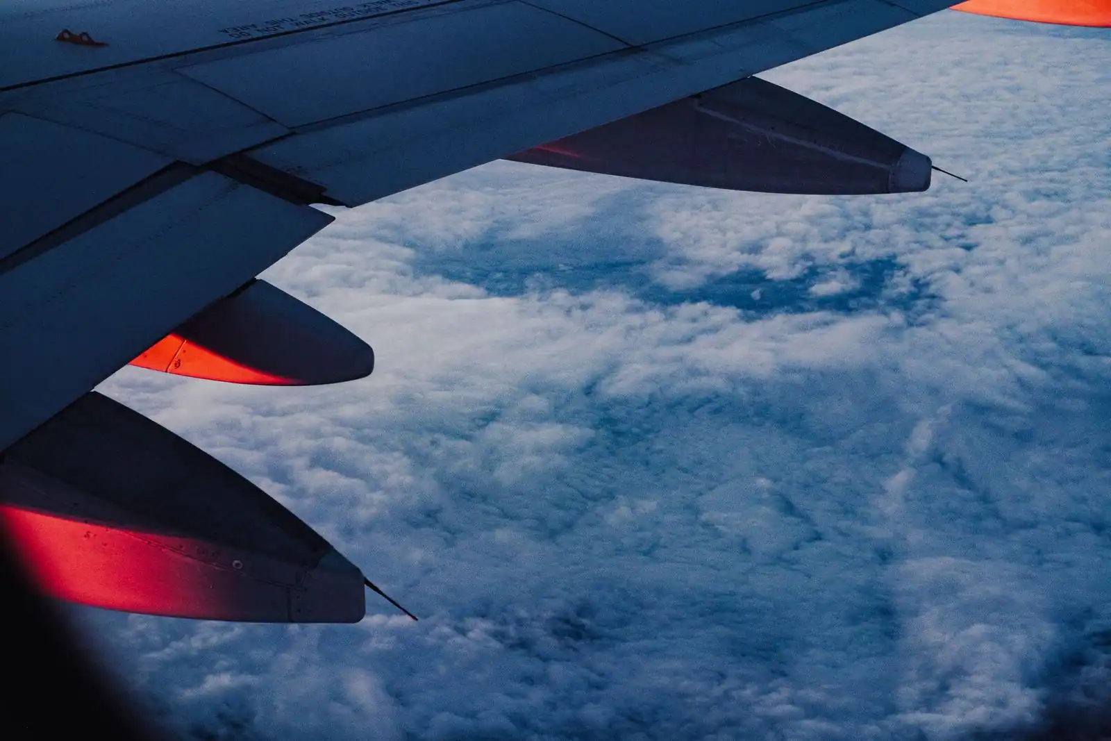 Aile d’un avion de ligne vue d’un hublot, au-dessus d’une épaisse couche de nuages au crépuscule
