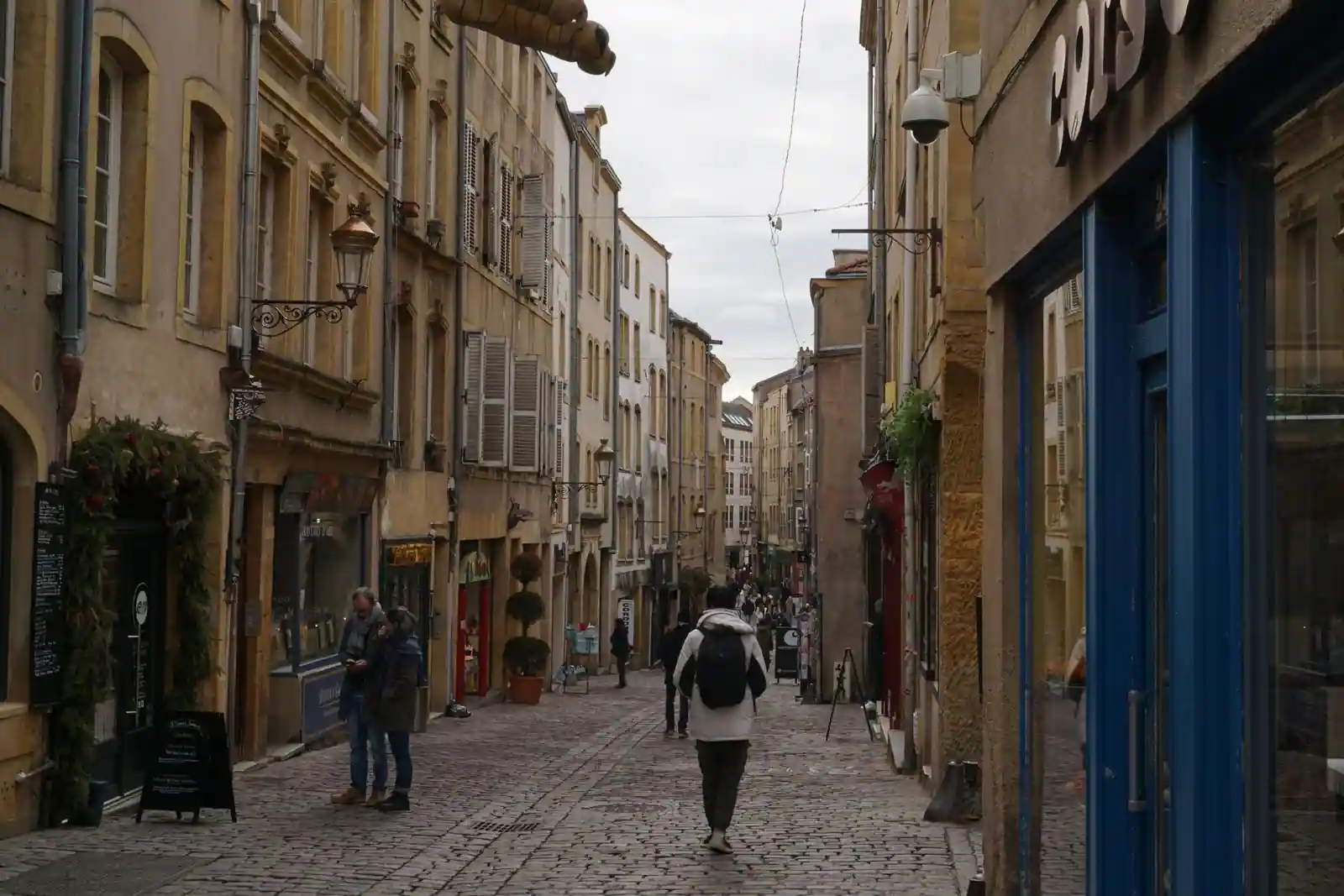 Ruelle pavée d’une vieille ville aux façades anciennes, où des passants flânent entre les commerces