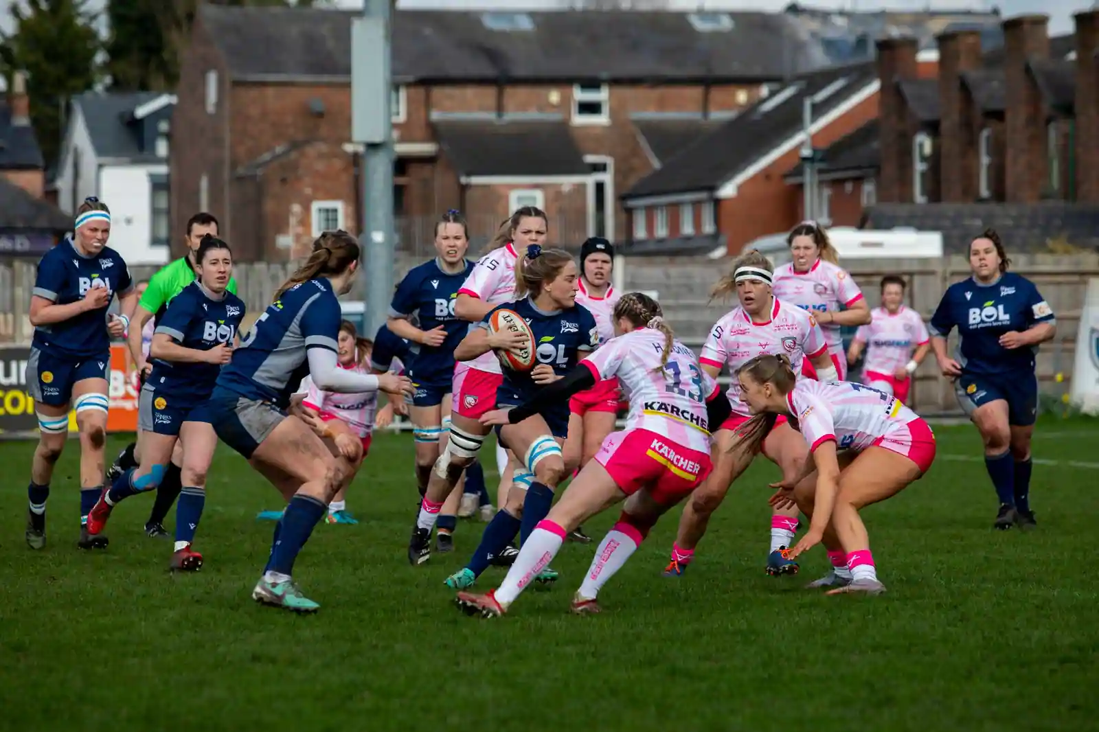 Des joueuses de rugby à XV portent le ballon lors d’un match sur un terrain herbeux, défense au contact.